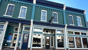 A two-story building with a green facade and white trim. It features a large entrance with glass doors and windows, and a sign above the door.
