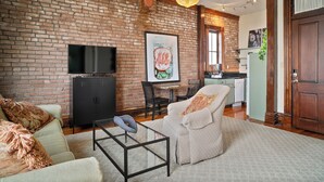 A living room with a brick wall, a flat-screen TV, a sofa, a coffee table, and a dining area with a table and chairs.