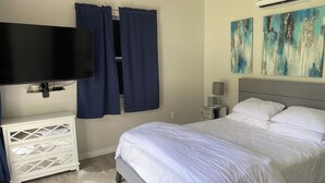 A bedroom with a bed, a TV mounted on the wall, a nightstand with a lamp, and artwork on the wall. - Private Lakefront Cottage, Bright, Peaceful, and Perfect for a Relaxing Escape. (Clermont)