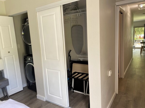 A laundry room with a washing machine, ironing board, and drying rack.