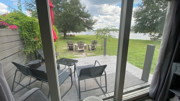 A room with a large sliding glass door leading to an outdoor patio with chairs and a table. - Private Lakefront Cottage, Bright, Peaceful, and Perfect for a Relaxing Escape. (Clermont)