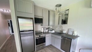 A modern kitchen with stainless steel appliances, white cabinetry, and a wooden floor. - Private Lakefront Cottage, Bright, Peaceful, and Perfect for a Relaxing Escape. (Clermont)