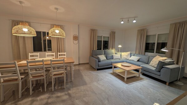 A modern living room with a dining area, featuring a sofa set, dining table, chairs, and pendant lighting.