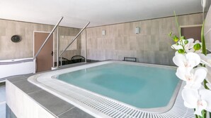 A modern indoor swimming pool with a tiled deck, a clock on the wall, and a staircase leading to an upper level.