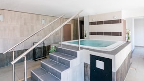 Piscina interior moderna con una escalera que lleva a una puerta, rodeada de paredes de azulejos y una barandilla de metal.