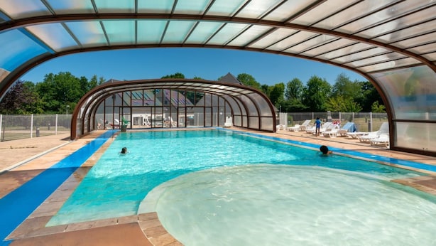 Una piscina interior con techo de vidrio, rodeada de sillones de descanso y una zona cubierta.