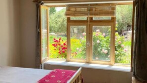 A bedroom with a wooden bed, a window with a view of a garden, and a wooden ceiling.