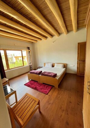 Une chambre spacieuse avec un grand lit, des poutres apparentes au plafond, un bureau en bois et une fenêtre donnant sur un paysage verdoyant.