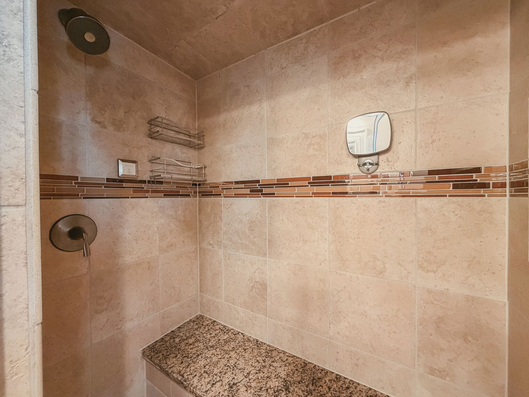 A bathroom with beige tiles, a granite countertop, a towel rack, a toilet paper holder, and a showerhead.