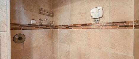 A bathroom with beige tiles, a granite countertop, a towel rack, a toilet paper holder, and a showerhead.