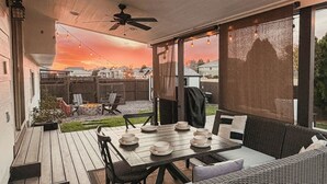 Een overdekt terras met een eettafel, buitenmeubels en uitzicht op de zonsondergang.