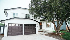 A two-story house with a garage, a tree in the front yard, and a small porch. - Modern 3BR: Fire Pit + Chef Kitchen + Skiing < 90 min + Near Red Rocks (Littleton)