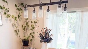 Een ronde eettafel met vier stoelen, een vaas met gedroogde bloemen en een hanglamp.