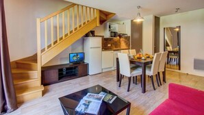 A modern apartment with a wooden staircase, a dining area with a table and chairs, a kitchen with a refrigerator and microwave, and a living area with a red sofa and a coffee table.