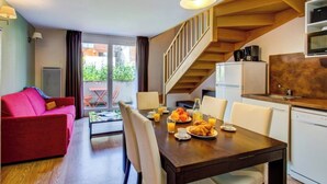 A modern living room with a wooden dining table set for breakfast, a red sofa, and a staircase leading to a kitchen.