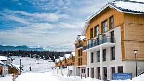 A hotel with a modern design, featuring multiple balconies and a ski slope in the background.