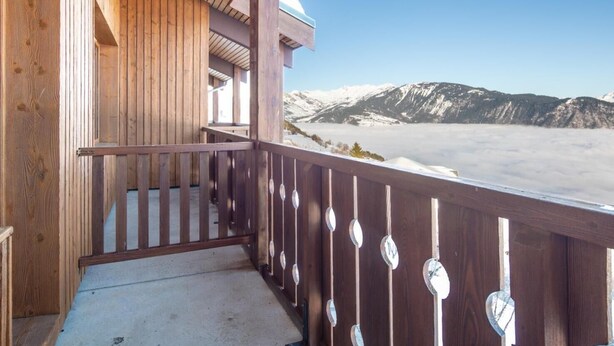 Ein Holzbalkon mit Blick auf schneebedeckte Berge und einen klaren Himmel.
