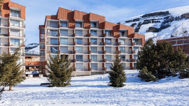 A multi-story hotel with balconies, surrounded by snow-covered ground and trees, with a mountain in the background.
