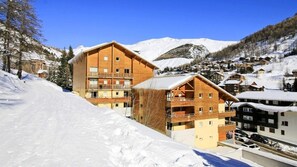 A wooden chalet-style hotel with multiple balconies, set against a snowy mountain backdrop.