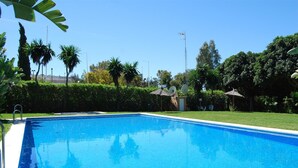 A rectangular swimming pool with a clear blue surface, surrounded by well-maintained grass and palm trees. - Apartment in Guadalmina Alta next to the Golf and shopping center. (San Pedro de Alcantara)