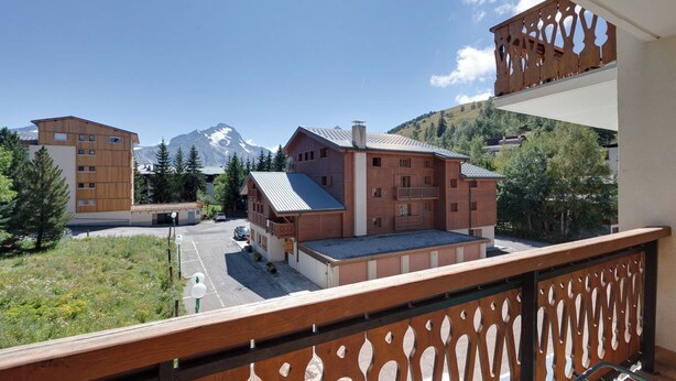 A mountain lodge with a wooden facade, a parking area, and a view of snow-capped mountains.