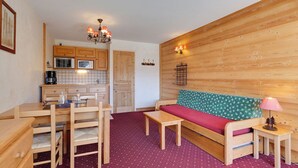 A cozy room with a wooden bench, a small table, and a kitchenette in the background.