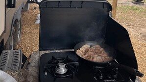 A portable gas stove with a pot of food, a covered area with a view of a lake, and a camper parked nearby. - Private Waterfront Camper with Dock and Boat Ramp on Weiss Lake (Cedar Bluff)