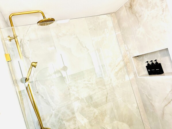 Un baño con ducha, toallero y repisa con artículos de aseo.