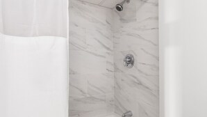 A shower with a marble wall and a showerhead. - Premium Double Queen Studio | The Beverly | Minutes to Peabody Essex Museum (Beverly)