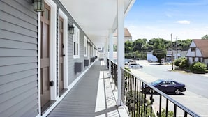 A covered porch with a railing, a row of doors, and a view of a street with parked cars.