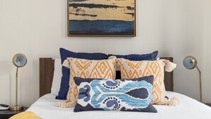 Un letto rifatto con cuscini a motivi decorativi, un quadro appeso sopra e due lampade ai lati.