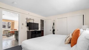 Ein Hotelzimmer mit einem großen Bett, einem an der Wand befestigten Fernseher, einem Kleiderschrank und einem Schreibtisch mit Stuhl.