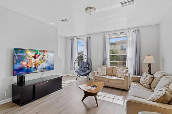 Una sala de estar moderna con televisor de pantalla plana, mueble de entretenimiento negro, sofá color beige, mesa de centro de madera y una silla colgante.