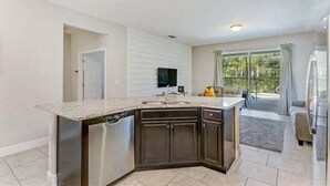 A modern kitchen with a built-in dishwasher, dark cabinetry, and a large window offering a view of the outdoors. - Solterra Swanky (Davenport)
