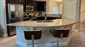 A kitchen with dark cabinets, stainless steel appliances, a granite countertop, and two bar stools. - Solterra Swanky (Davenport)