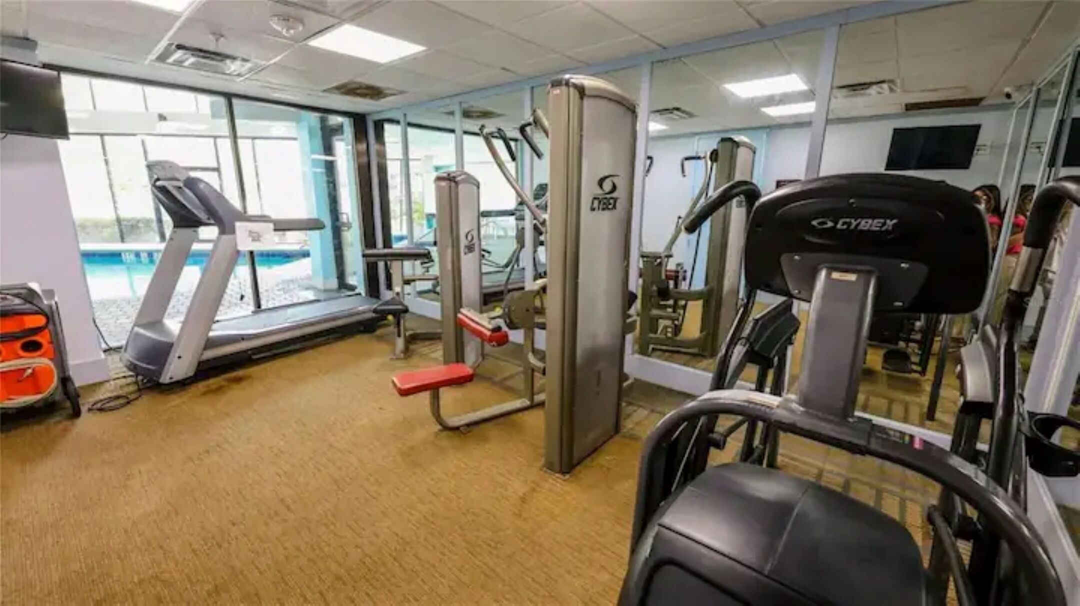 A gym with cardio machines, weight training equipment, and a large mirror.