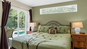 Un dormitorio con una cama grande, dos mesitas de noche con lámparas, una ventana con persianas y vistas a una piscina exterior.