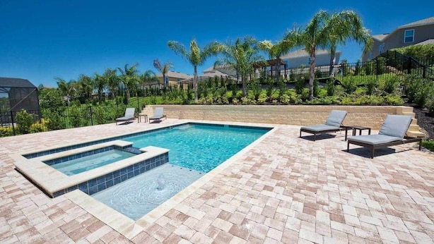 A rectangular swimming pool with a hot tub, surrounded by a brick patio with lounge chairs. - Encore Swanky (Kissimmee)