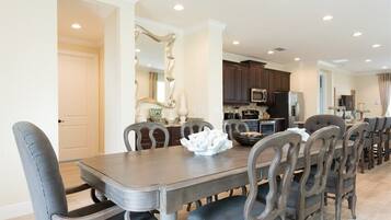 A dining area with a wooden table and upholstered chairs, a kitchen with dark cabinets and stainless steel appliances, and a decorative mirror.