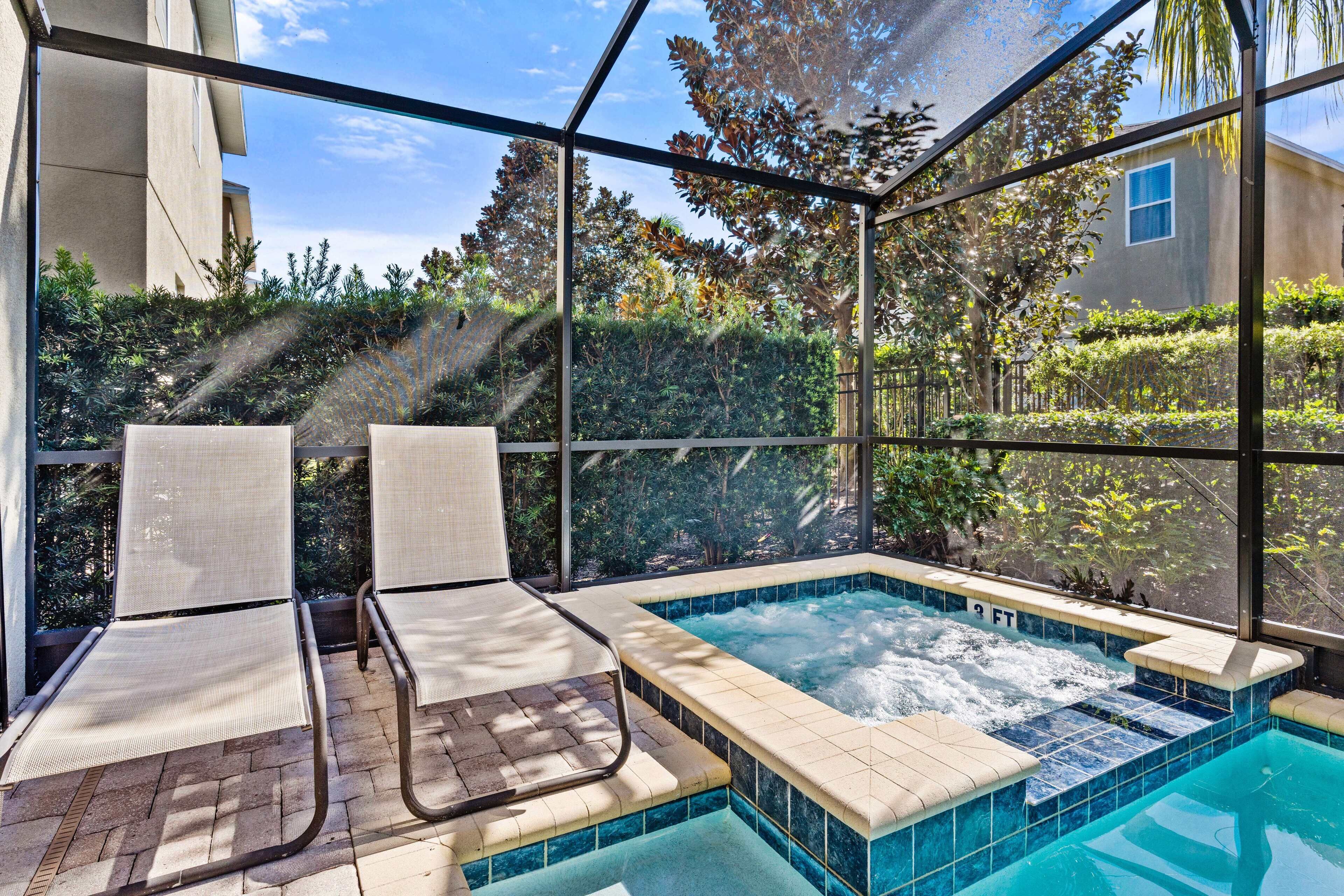 A glass-enclosed outdoor pool area with two lounge chairs and a hot tub.