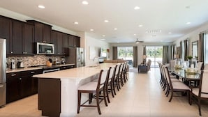 A spacious kitchen with dark cabinets, a central island, and a dining area with chairs and a table. - Encore Swanky (Kissimmee)