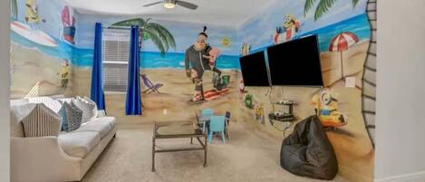 A room with a beach mural, a white sofa, a coffee table, a TV, and a ceiling fan.