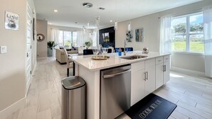 A modern kitchen with a central island, stainless steel appliances, pendant lighting, and a view to the outdoors. - Reunion Swanky (Kissimmee)