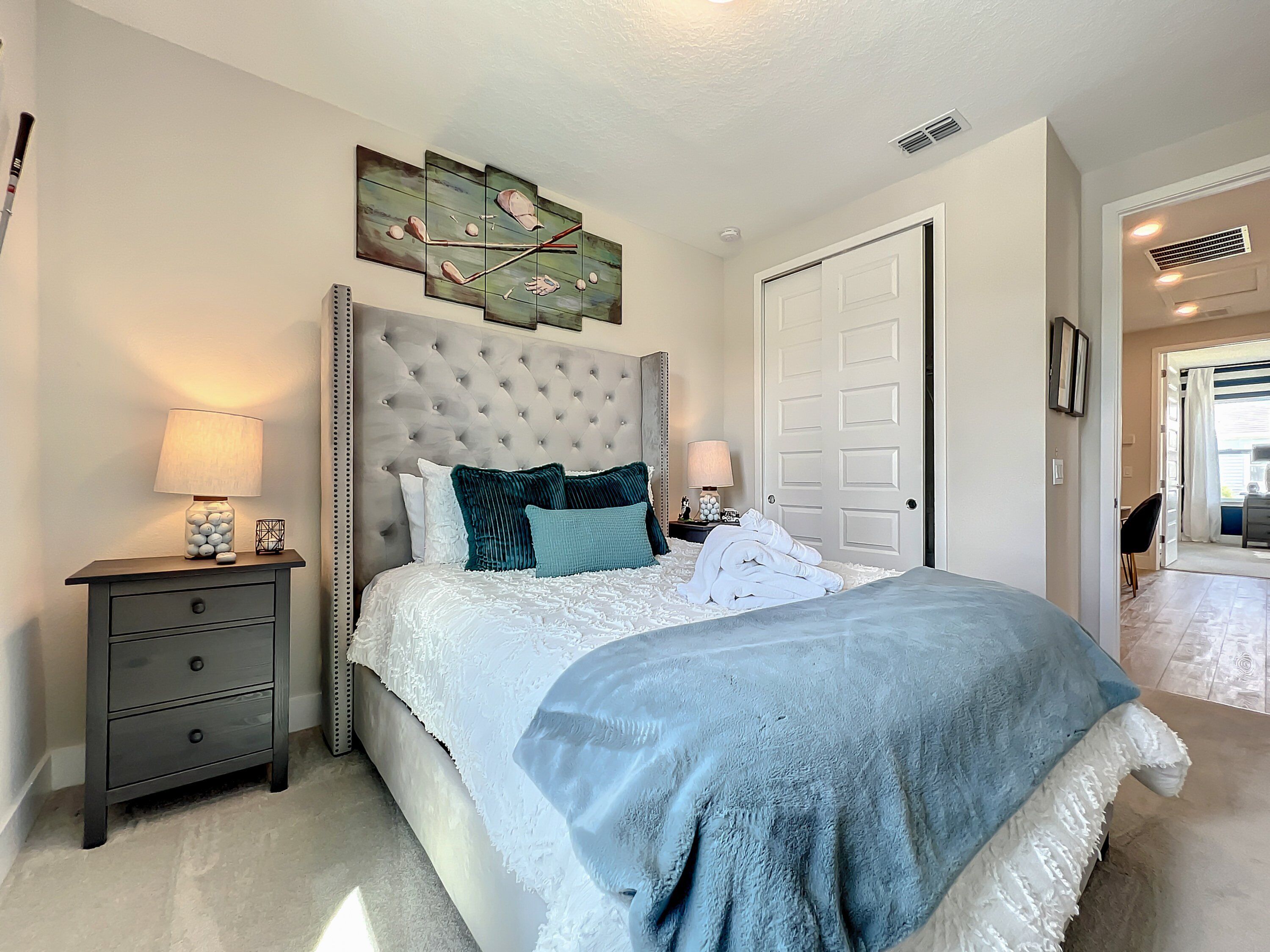 A bedroom with a tufted headboard, a large bed with white linens, two bedside tables with lamps, and a door leading to another room.