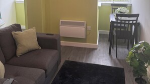 Una sala de estar con un sofá, una mesa de comedor con sillas, un reloj, aire acondicionado y una ventana con persianas.
