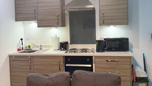 Una cocina moderna con armarios de madera, estufa, microondas y pileta. Se observa un sofá en primer plano.