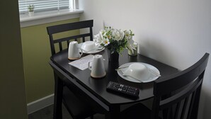 Una mesa de comedor con sillas, un control remoto, un florero con flores y un cuadro en la pared.