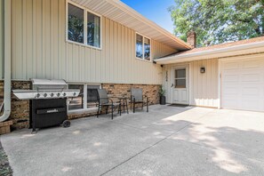 Uma casa com espaço para churrasco, incluindo uma churrasqueira e cadeiras, e uma porta de garagem.