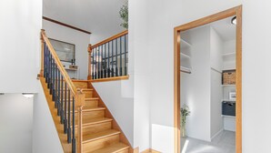 Una escalera con peldaños de madera y barandillas negras que conduce a una habitación con paredes blancas y suelo de baldosas.
