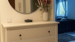 A bedroom with a white dresser, a round mirror, and a vase with dried plants. - Charming apartment with terrace and parking space near the Rhine and Bonn city center (Bonn)